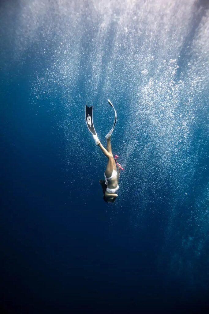 anonymous female diver swimming under blue ocean in sunlight