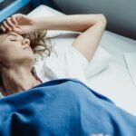 Adult woman sleeping on bunk bed with blue blanket in a hostel.