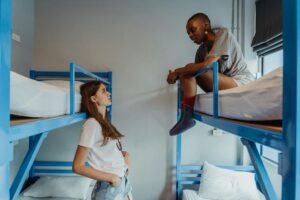 Two young women engaging in conversation in a casual hostel setting with blue bunk beds.